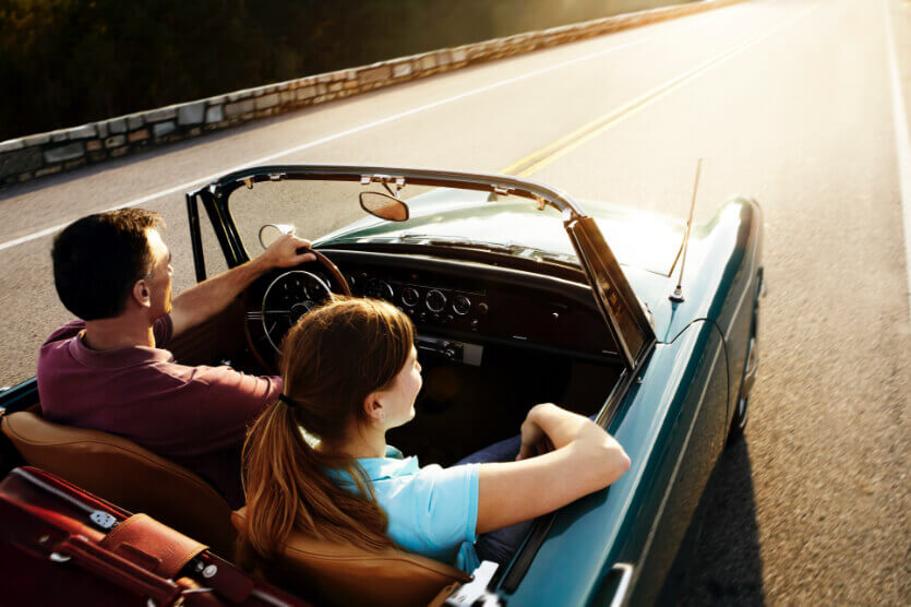ima-classic-car-lg Male and female in convertible classic car driving on the highway